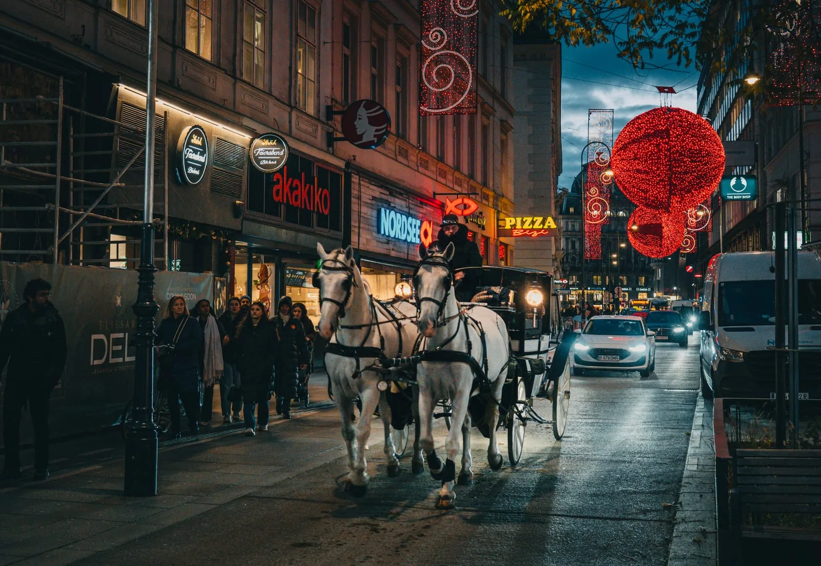 Two white horses pulling a Fiaker at night on Kärntner Straße with Christmas lights, Vienna